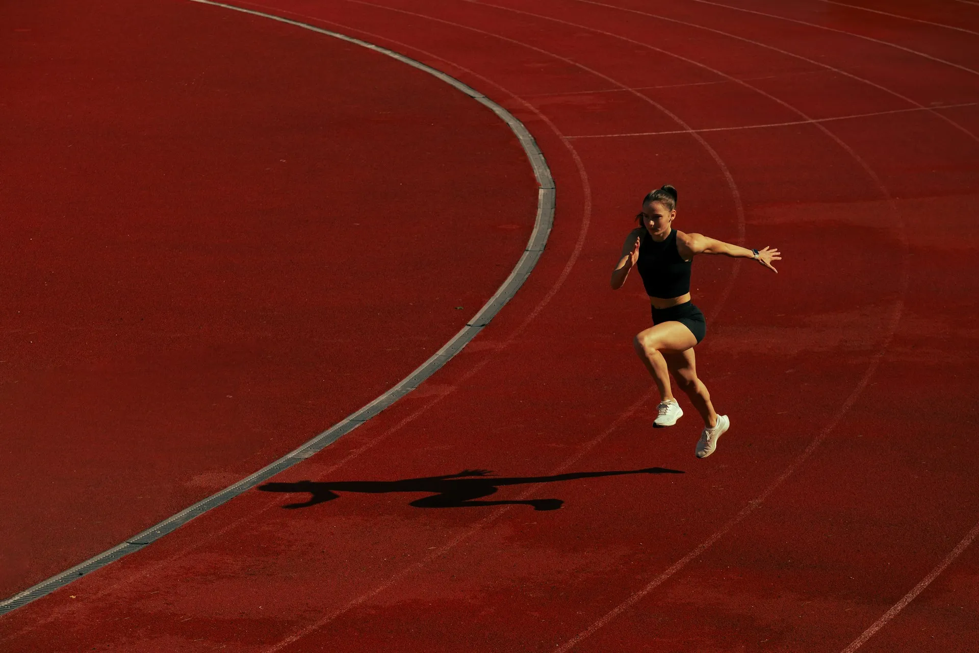 A sprinter bounding along a red running track in low sun.