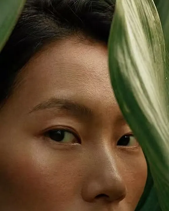 A close portrait, half the face behind a broad green leaf.